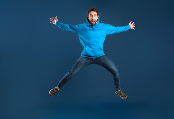 Fototapeta na wymiar Crazy Offer. Funny Young Man Jumping Like A Star Over Blue Background