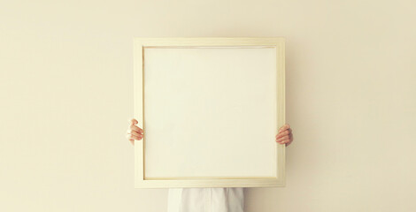 Woman decorating interior, hanging white blank photo frame, wooden picture on wall in new house