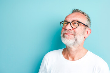 An elderly caucasian man with glasses and a white beard looking sideways, isolated on light blue background.