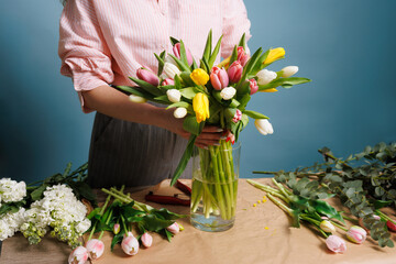 girl florist collects a bouquet of spring tulip flowers on a clean blue background