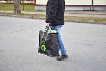 A man carries a black bag with plastic bottles to hand over.