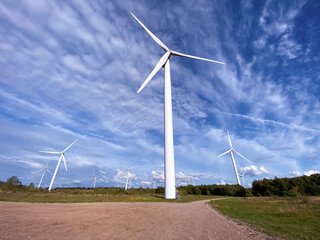 Fototapeta premium Windmill farm among fields and small trees. European Environment Initiative. Conservation of energy and fossil resources. Zero Ecological Footprint