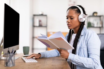 Focused black female student with headphones reviewing notes while using computer