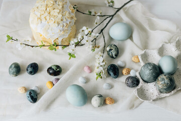 Stylish easter eggs, panettone and spring flowers on linen cloth on rustic table. Natural dye eggs...