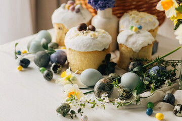 Stylish easter eggs, panettone, spring flowers and chocolate eggs on rustic wooden table. Natural...