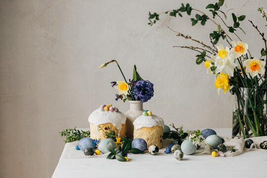 Happy Easter! Stylish easter eggs, homemade easter bread and spring flowers on linen napkin on rustic table. Natural painted marble eggs, daffodils bouquet and holiday food. Modern still life