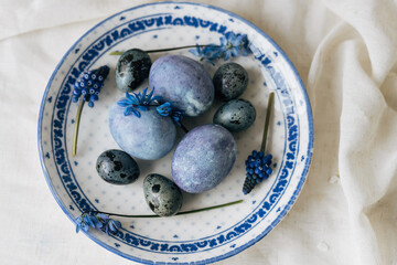 Stylish easter eggs on vintage plate and spring flowers on rustic table. Happy Easter! Natural dye...