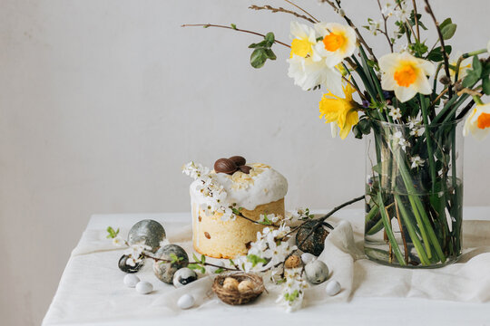 Happy Easter! Stylish easter eggs, homemade easter bread and spring flowers on linen napkin on rustic table. Natural painted marble eggs and daffodils bouquet, minimal still life
