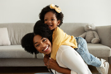 Happy young black mother lifting up her pretty little daughter