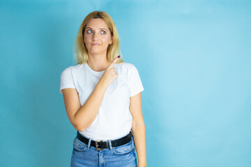 Fototapeta na wymiar Young beautiful woman wearing casual t-shirt over isolated blue background confused and pointing with hand and finger to the side