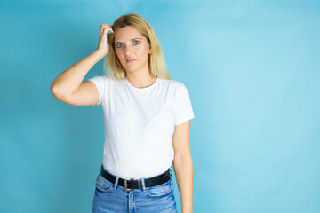 Young beautiful woman wearing casual t-shirt over isolated blue background confuse and wonder about...
