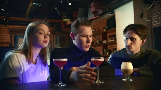 Group of friends are sitting at bar and drinking cocktails. Media. Friends drink at bar for weekend meeting. Friends chat and drink cocktails in abra on weekend