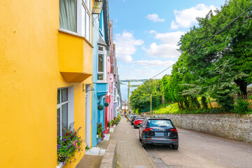 View from the top of the street of the picturesque and colorful Deck of Cards, a row of brightly painted townhomes, in the coastal town of Cobh, Ireland, Cork County.	