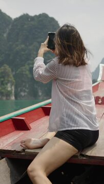 In a wooden boat a woman takes pictures of the lake