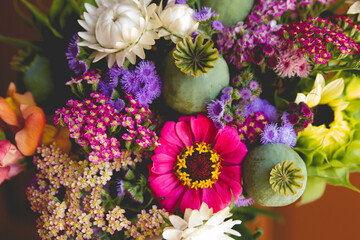 Closeup of a mixed summer flower bouquet with poppy pods, sunflowers, zinnias, yarrow and ageratrum