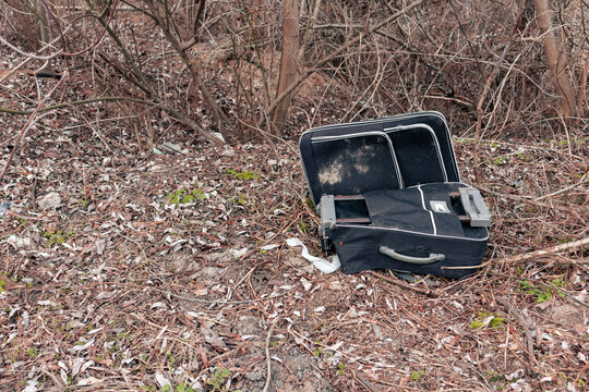 An old and torn traveler suitcase lies in the forest
