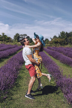 A couple in love, a man and a woman, are walking in a lavender meadow. The man lifted the woman in his arms, they look at each other and smile. A summer walk of a young couple through a lavender fiel.