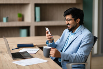 Successful Middle Eastern businessman enjoying coffee texting on cellphone indoor