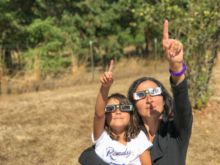 Mother and daughter, family viewing solar eclipse with special glasses in a park - 755112142