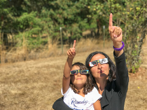 Naklejki Mother and daughter, family viewing solar eclipse with special glasses in a park