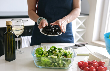 Woman At Home Prepares Greek Salad, Pouring Olives Into Salad Bowl - 755112311