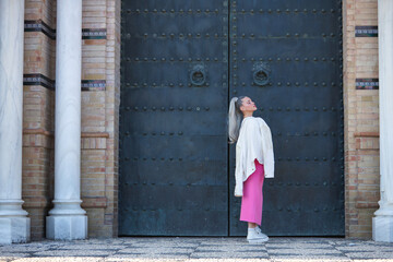 Young, pretty, blonde woman with eyes closed, fringed jacket on the shoulder and pink skirt posing...