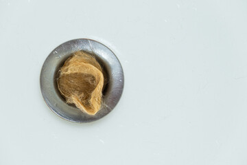 hand detail of a large tuft of hair clogging the drain of a white bathtub. overhead view. Hair loss. cleaning the bathroom.