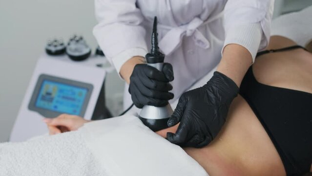  A cosmetologist utilizes an ultrasound device during a lifting procedure on a woman's abdomen