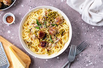 Spaghetti with meatballs and cream sauce is served on a plate with herbs and parmesan.