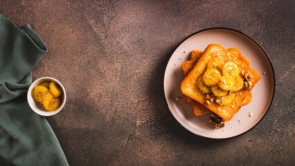 Caramelized bananas with nuts on fried bread on a dessert plate on the table top view web banner