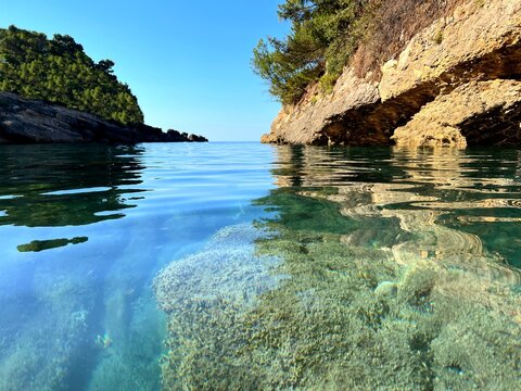 Sea bay with clear water on pebbly beach and coastal rocks.