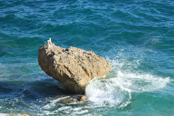Piedra en medio de mar con oleaje y un montículo de piedras pequeñas encima