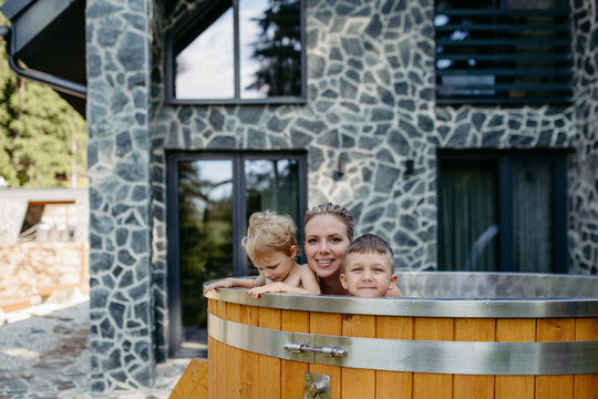 Mother with two kids playing in the water, in outdoor hot tub. Brother and sister enjoying summer time in outdoor pool, having fun with single mom.