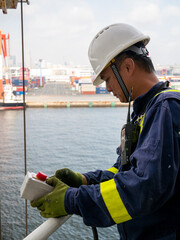 Seaman crew member of cargo vessel  equipped with personal protective equipment operate life boat davit  on the cargo ship in helmet with walkie talkie.