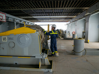 Seaman crew member of cargo vessel  equipped with personal protective equipment is doing maintenance painting of mooring winch on aft station