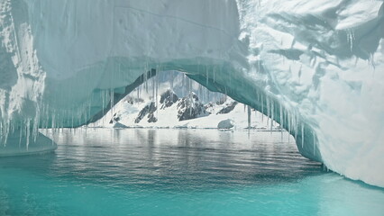 Close up iceberg arch at turquoise ocean bay with mountains on snowy shore aerial. Arctic...