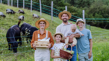 Portrait of farmer family holding harvest basket full of fresh vegetables, in front of paddock. Concept of multigenerational and family farming.