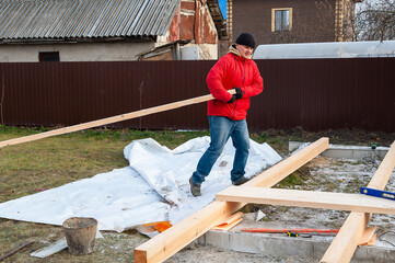 A man in a red jacket is engaged in construction using wooden planks - 755144327