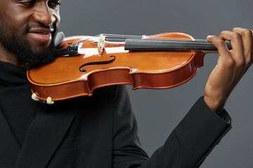 Elegant African American man playing a violin in black suit on gray background