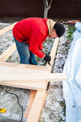 A man in a red jacket is engaged in construction using wooden planks