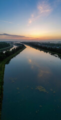 This image depicts the quiet splendor of dawn as it breaks over a serene waterway. The sky, painted...