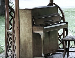 Stare pianino stoi w parki. Elegancki fortepiany postawiony na świeżym powietrzu dla przechodniów. Zabytkowy instrument, krzesło i osłona z drewna. - obrazy, fototapety, plakaty