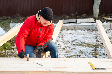 A man in a red jacket is engaged in construction using wooden planks - 755149368