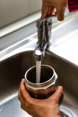 Unrecognizable hands filling a coffee pot with water at the kitchen sink faucet to make coffee.