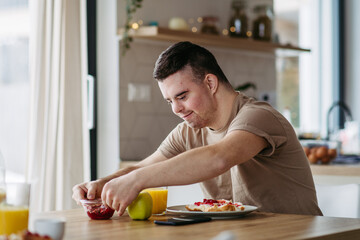 Young man with Down syndrome preparing breakfast on his own. Morning routine for man with Down...