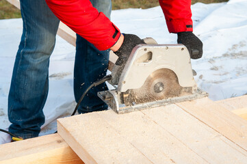 A man in a red jacket cuts boards with a circular saw - 755150578