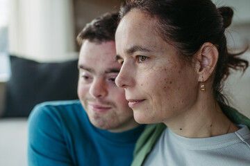 Portrait of young man with Down syndrome with mother at home, holding, touching with foreheads. Concept of love and parenting disabled child.