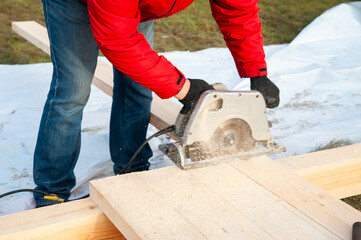 A man in a red jacket cuts boards with a circular saw - 755150995
