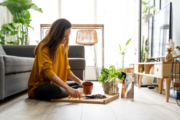 Young Caucasian woman pouring soil into a pot to plant cuttings.