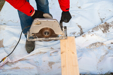 A man in a red jacket cuts boards with a circular saw - 755152714